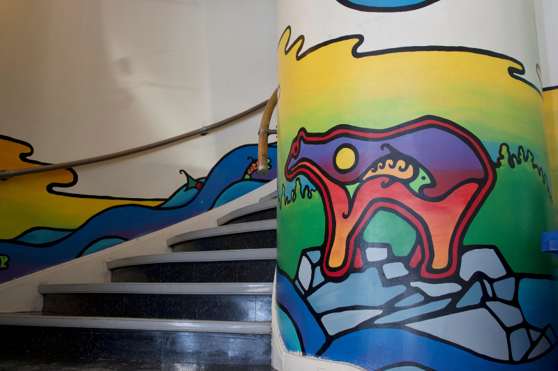 The painted stairwell of First Nations House at UofT. There is a mural of a bear and some fish running upstream.