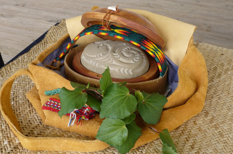 The mauri stone along with additions from other IILF conferences, including a wooden case, beaded band, deer hide, purple lining, possum skin and eagle feather with 8 silver beads